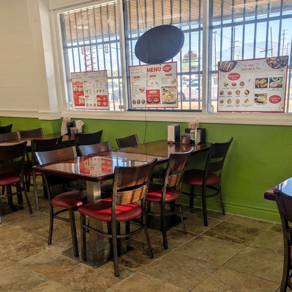 Bright Vietnamese restaurant dining area with wood tables, red-cushioned chairs, green walls, and menu boards lining the windows.